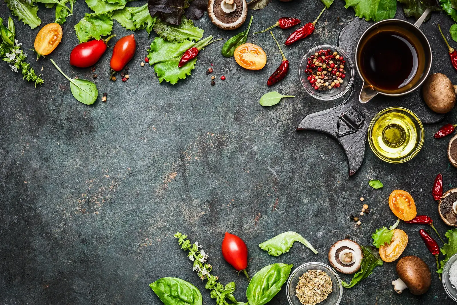 Fresh vegetables, herbs and olive oil arranged on a dark surface